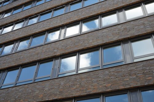 Eine Nahaufnahme der Backsteinfassade eines Bürogebäudes mit vielen Fenstern, in denen sich der Himmel spiegelt. Das Bild steht für die soliden Immobilien-Kapitalanlagen der Pensionskasse der Hamburger Hochbahn Aktiengesellschaft -VVaG-.