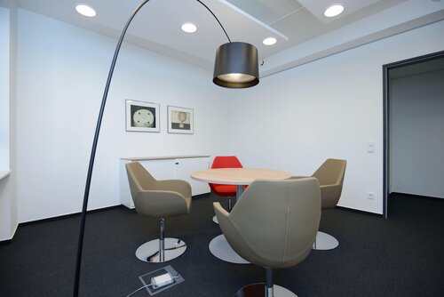 Ein moderner Besprechungsraum mit einem runden Tisch, vier Sesseln und einer großen Stehlampe. Ein Bild der Büroräume der Pensionskasse der Hamburger Hochbahn Aktiengesellschaft -VVaG-.
