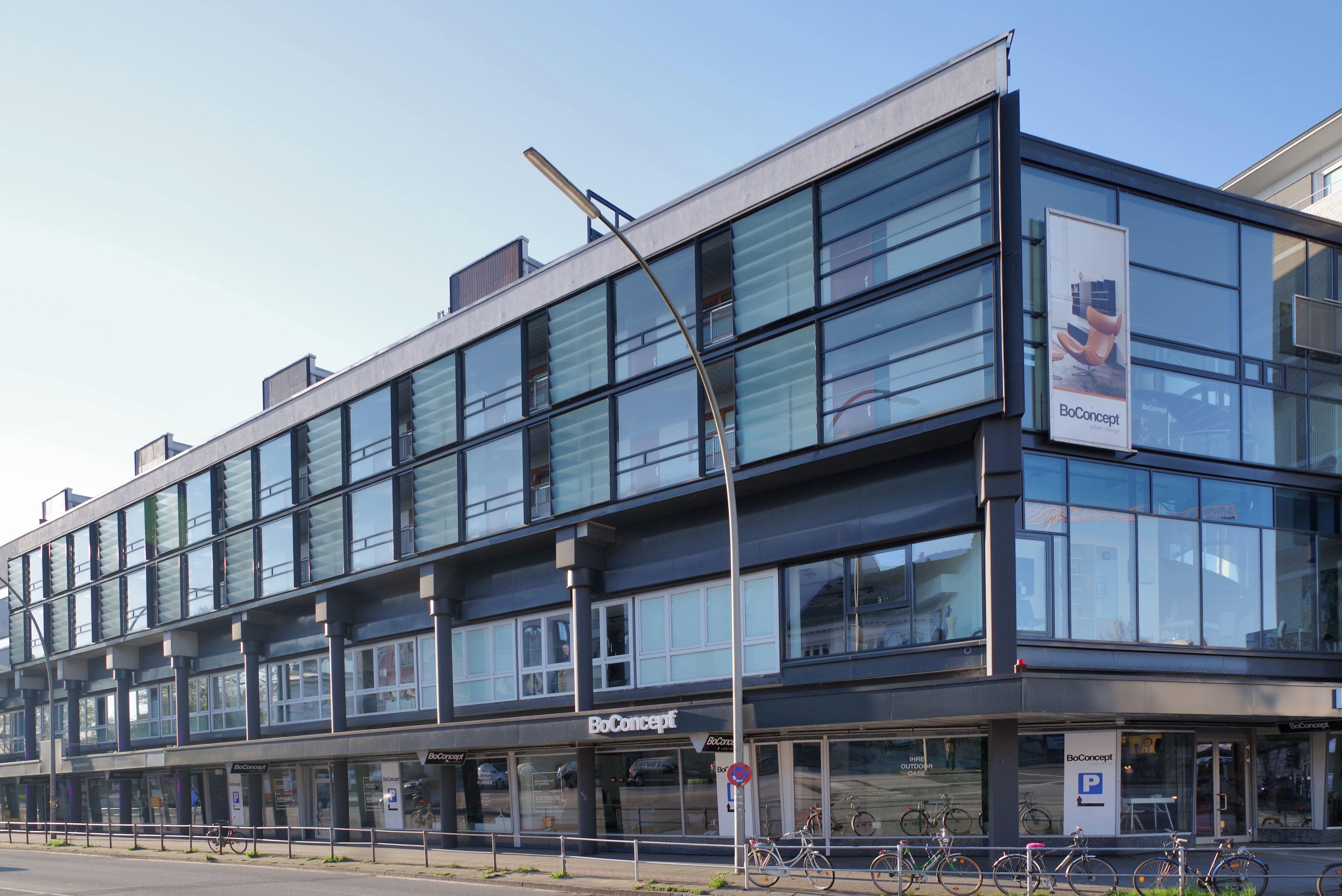 Modernes Bürogebäude mit großen Glasfronten und der BoConcept-Filiale im Erdgeschoss. Das Gebäude ist der Sitz der Pensionskasse der Hamburger Hochbahn Aktiengesellschaft -VVaG- und steht für ihre zukunftsfähige Ausrichtung.