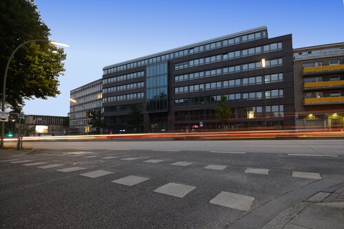 Das Bürogebäude der Pensionskasse der Hamburger Hochbahn Aktiengesellschaft -VVaG- bei Nacht, mit Lichtspuren von Autos auf der Straße.